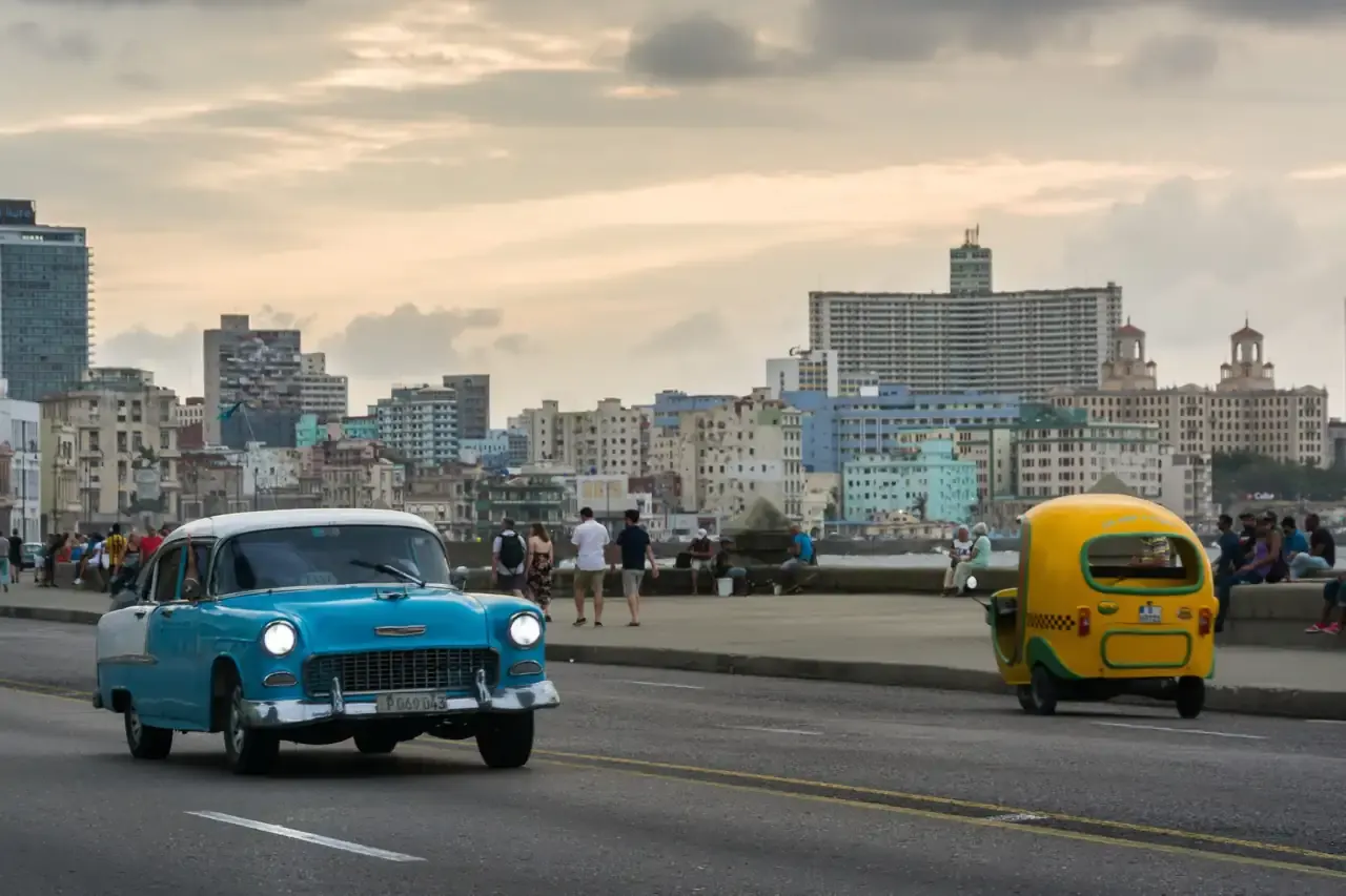 Un almendrón turquesa y un cocotaxi amarillo recorren el Malecón de La Habana al atardecer